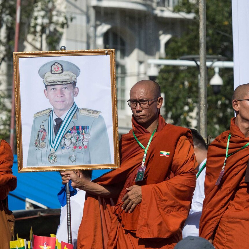 two monks in saffron robes carry large portraits of Myanmar's military commander-in-chief Min Aung Hlaing on stage