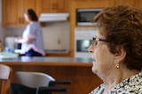  Bell Cares client Joan Hunter sitting in her dining room while her carer Sarah Heathwood washes the dishes