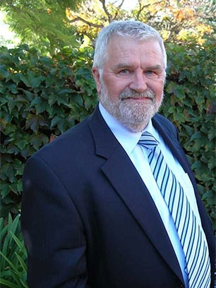 A man with grey hair and a beard wearing a suit and tie