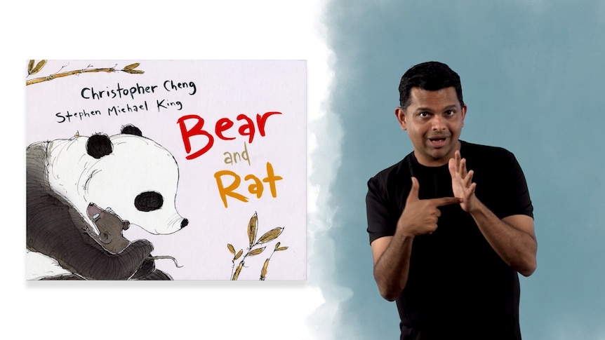 Auslan presenter Karthik Vijayanandam stands beside book called 'Bear and Rat'