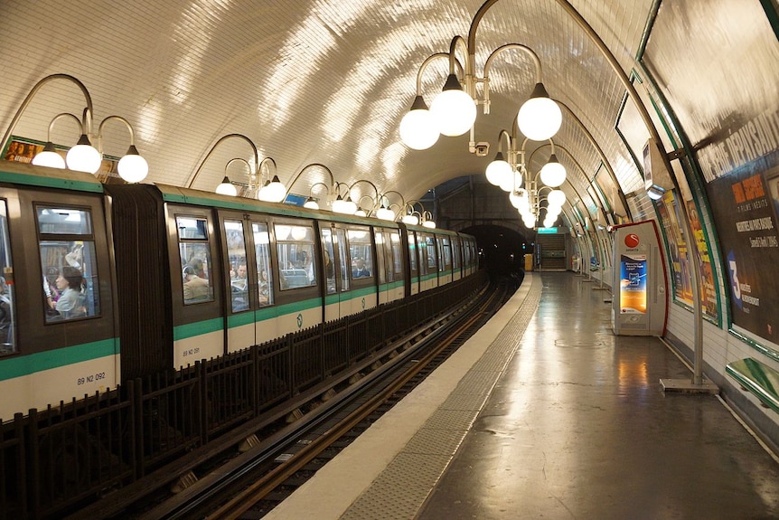 A historic Paris metro subway station, Cite, is pictured with a train stopped picking up passengers along a curved track.