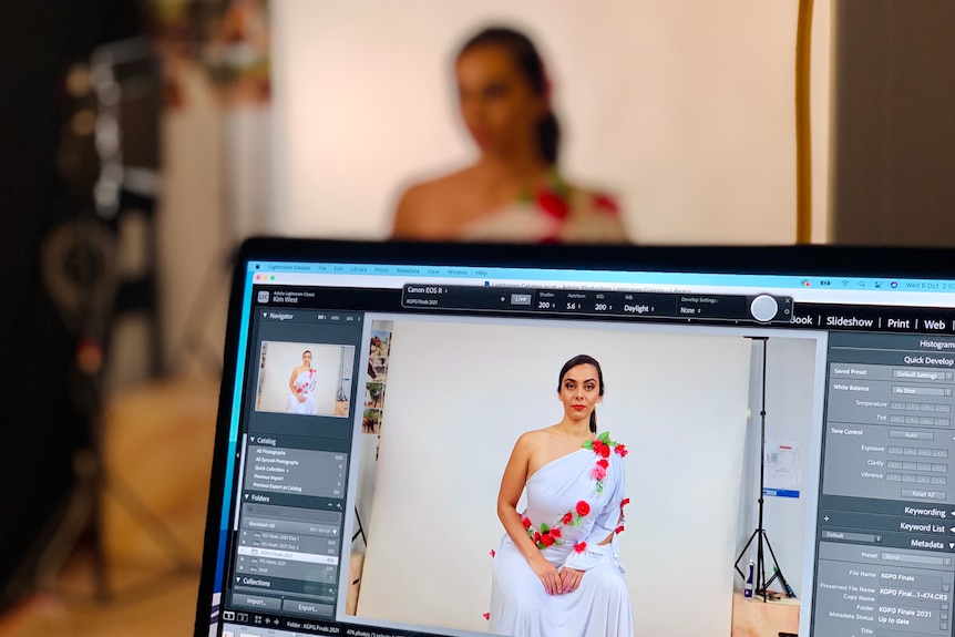A computer screen shows a young women modelling a white dress.
