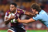 Filipo Daugunu holds a rugby ball under one arm and holds a player in a blue shirt with the other