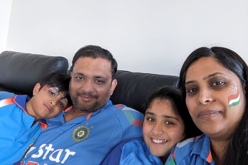 An Indian family in blue, with parents and a boy and girl, cuddle on their couch at home