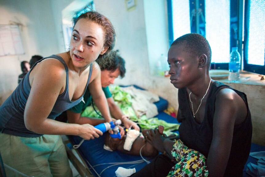 Nurse Jessica Hazelwood administers breaths to baby Nyanene, whose mother is staring into the distance.