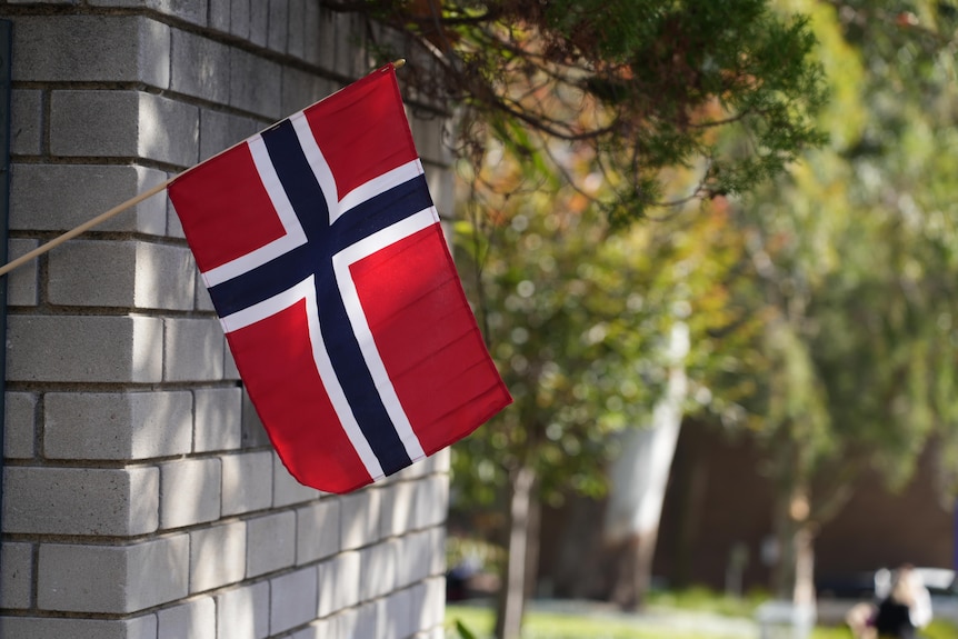 A Norwegian flag hangs from a brick wall.