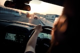 A photo of a person driving a car at sunset, taken from behind the driver's seat