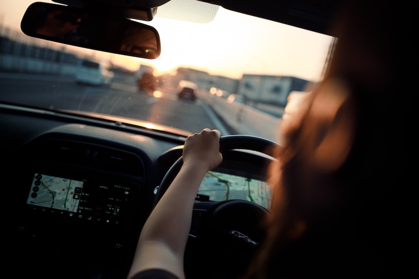 A photo of a person driving a car at sunset, taken from behind the driver's seat