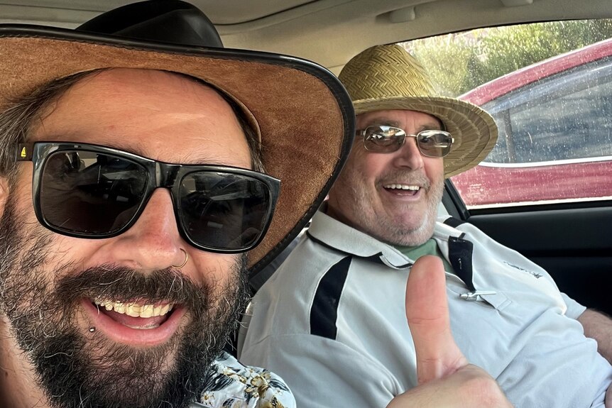 two men smiling at the camera taking a selfie inside a car