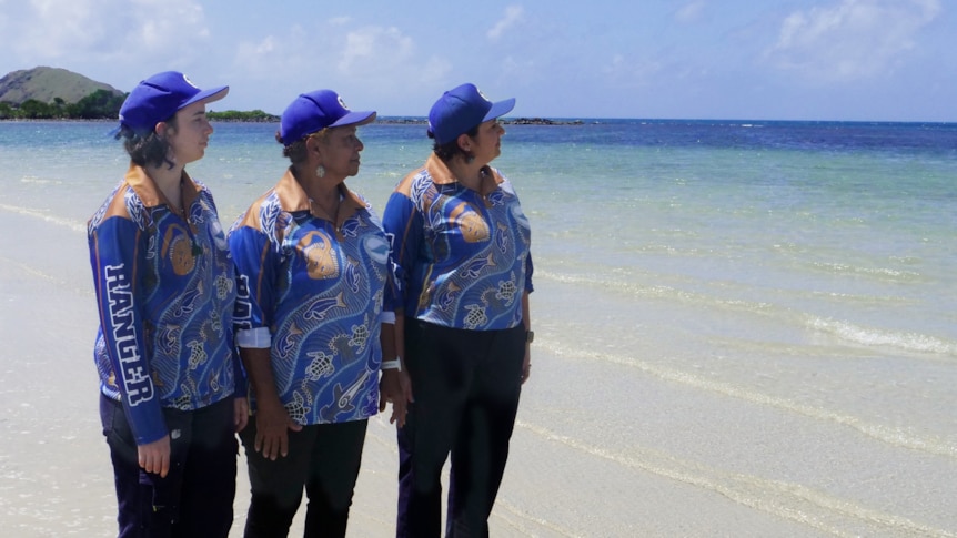 Three Indigenous women standing on a beach looking out to sea