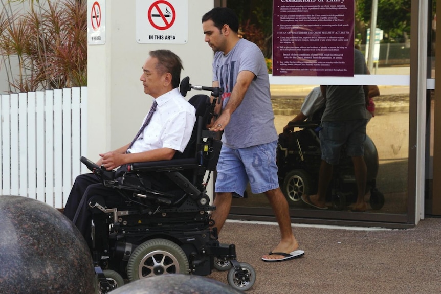 Partap Singh walks out of Darwin Local Court pushing a man on a wheelchair.