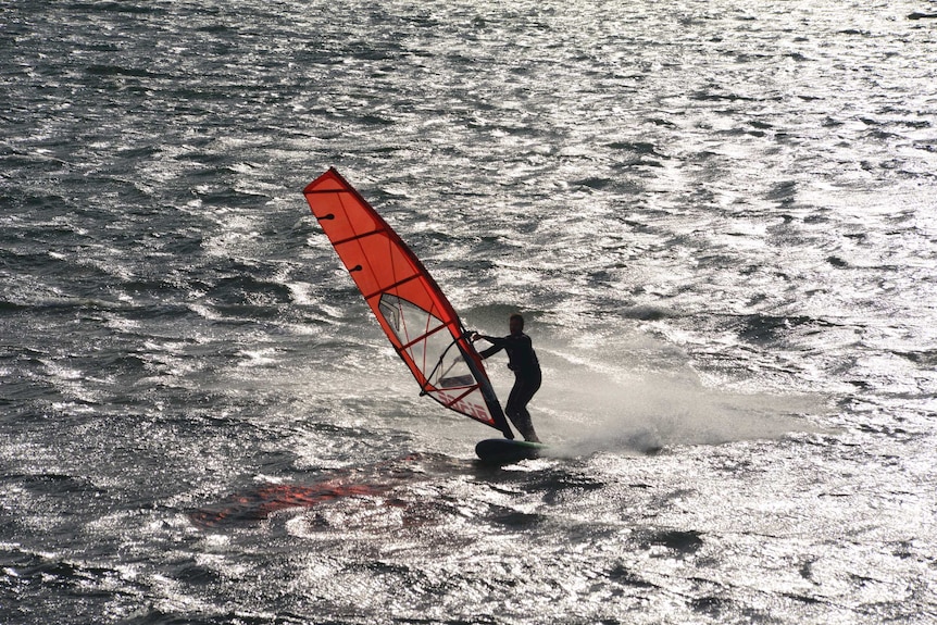 A man on an orange windsurfer on Port Phillip Bay.