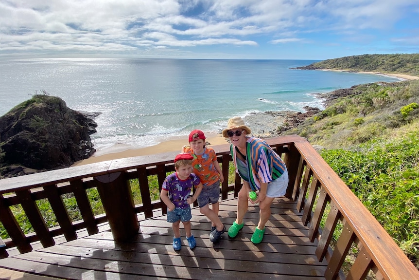 A mother and two sons standing at a lookout with the ocean behind them