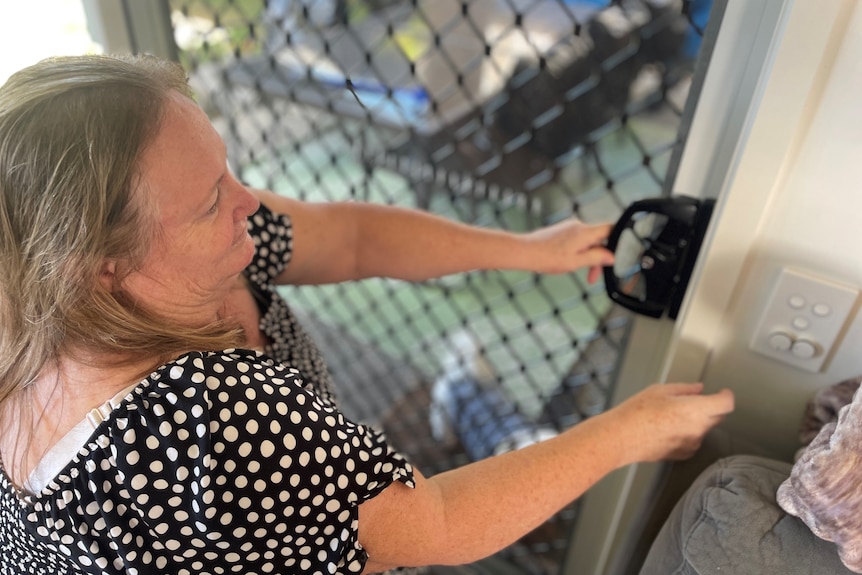 A woman in a black and white polka dot dress closing a sliding glass door. 