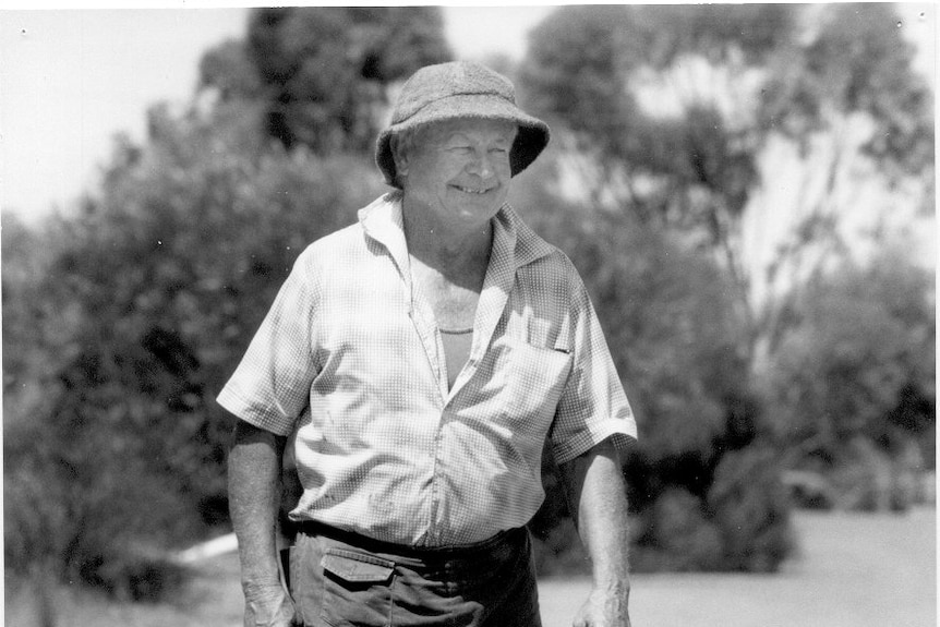 A black and white image of a smiling man in a bucket hat and a flannel t-shirt.