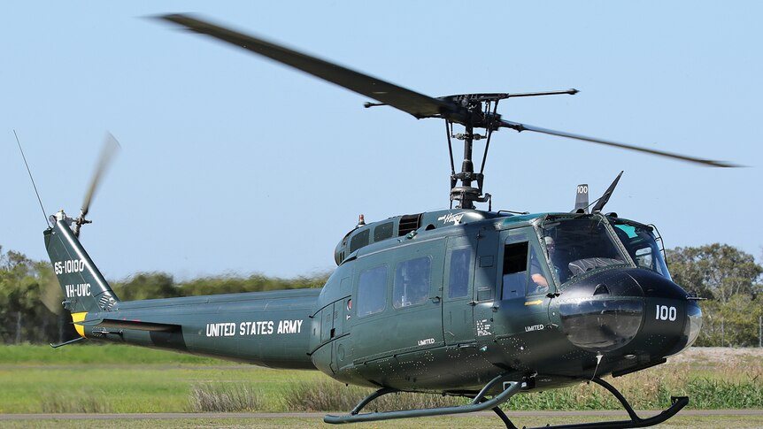 A military-style helicopter hovering just above the ground.