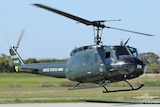 A military-style helicopter hovering just above the ground.