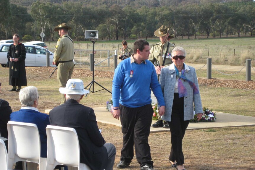 An older woman walking with a younger man during an army commemoration service.