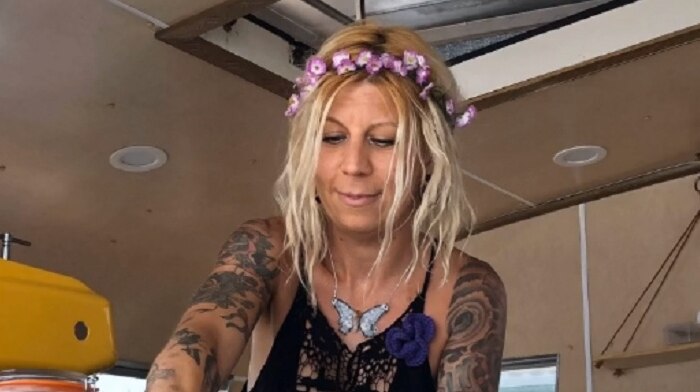 A blonde woman with a lei in her hair serves coffee from her caravan