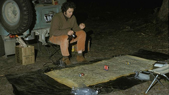 A man with recording gear sits in front of sheet with a grid on it, watching frogs.