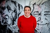 Fiona McKenzie stands in a red jumper in front of a black and white mural of a dog and a man, and she smiles at the camera.