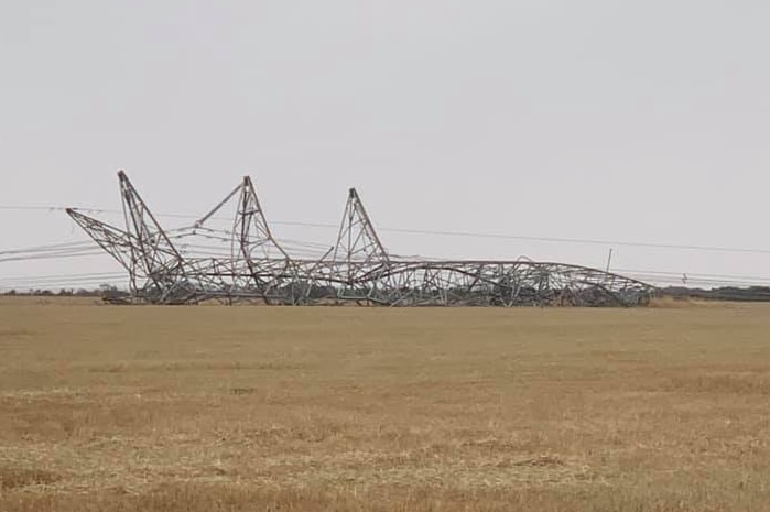 A power transmission tower lies collapsed on a field.