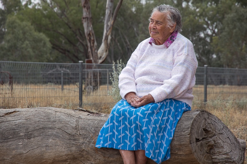 An older Aboriginal woman sitting on a log looking into the distance