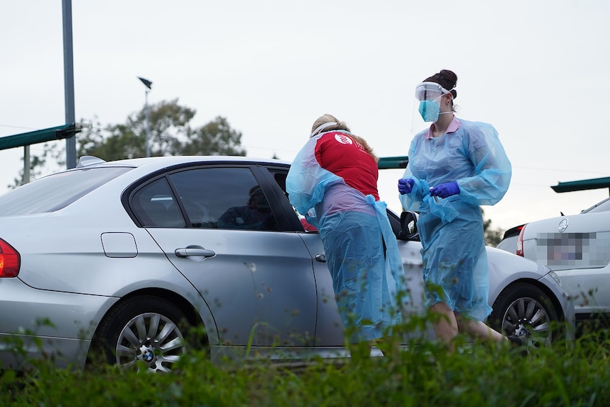 Two health workers next to cars lined up at COVID-19 testing drive-through clinic at Toowong in Brisbane