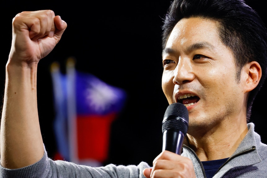 Close up of man speaking into microphone as he raises his fist in sign of victory.