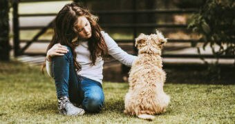 A girl sits on the lawn next to her dog