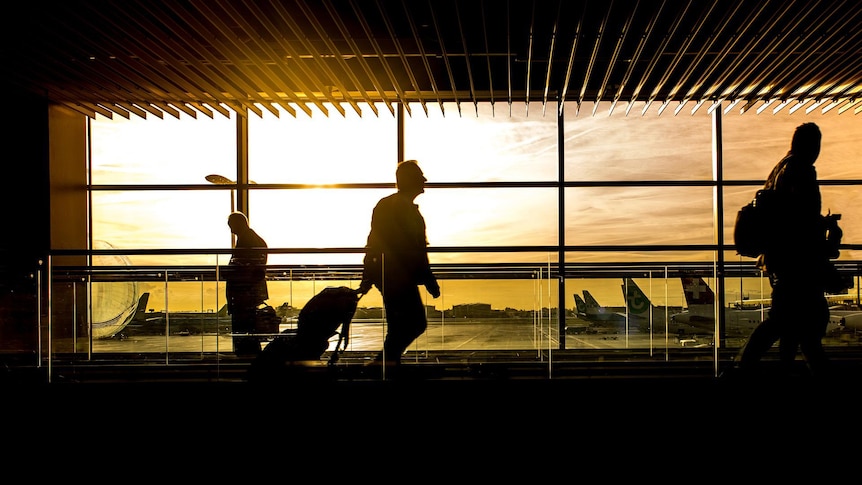 Passengers in airport concourse with planes on tarmac.