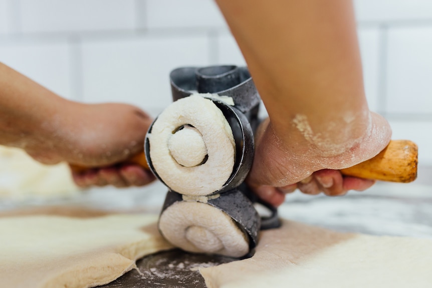 A close-up of hands using a doughnut cutter to cut out doughnut shapes from dough.