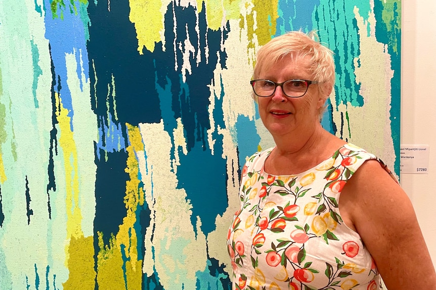 A woman stands in front of an abstract painting.