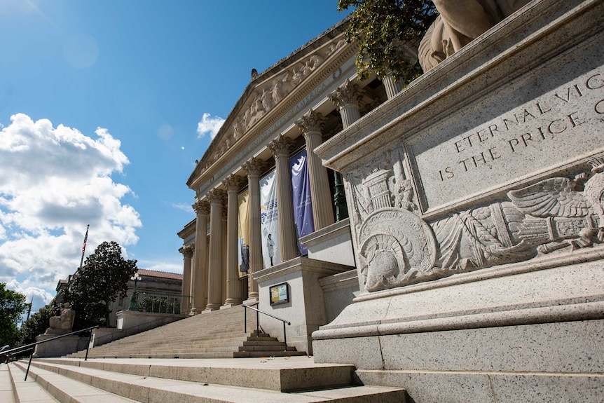 A classical stone building with composite columns and a triangular frieze sits at the top of a wide staircase.