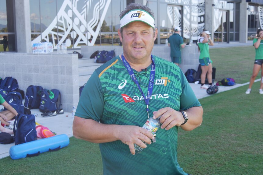 Middle-aged man in green shirt standing with water bottle in hand.