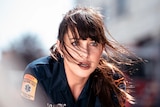 A brunette woman in a paramedic uniform looks up in shock in an action shot from Madame Web.