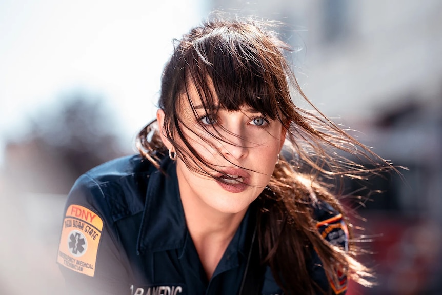 A brunette woman in a paramedic uniform looks up in shock in an action shot from Madame Web.