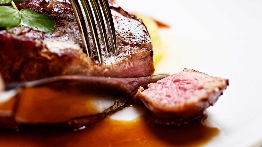Knife and fork slice into rare grilled steak