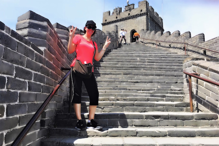 A young woman makes peace signs with her hands while posing for a photo on the Great Wall of China.