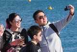 A group of four tourists stand on a jetty taking a selfie on Rottnest Island with the ocean behind them.