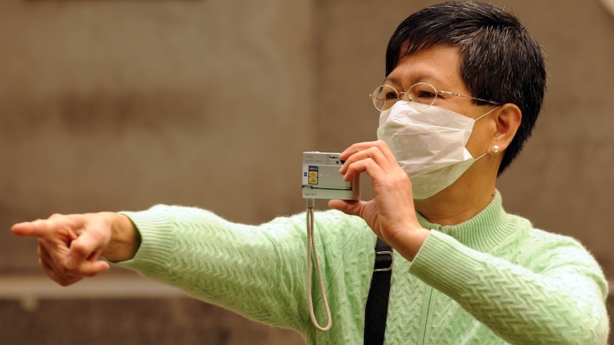 A woman points her finger, with a mask on her mouth