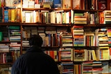 Person in bookshop with shelves full of colourful books.