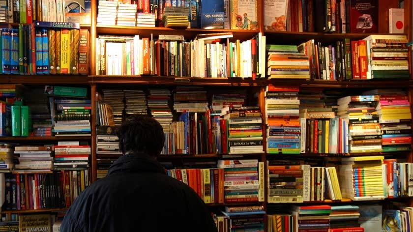 Person in bookshop with shelves full of colourful books.