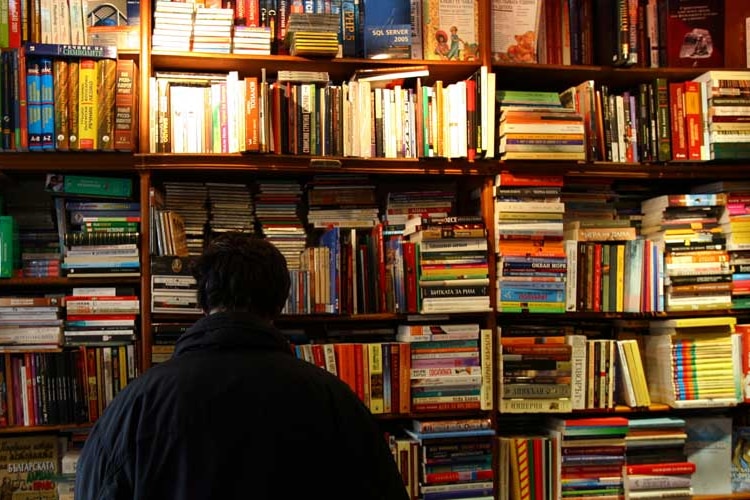 Person in bookshop with shelves full of colourful books.