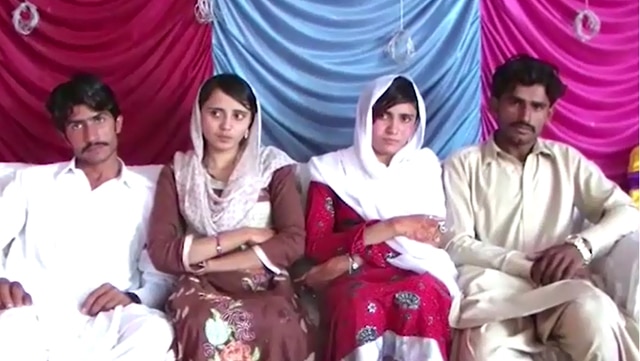 Two girls in head scarves sit on the couch with two men in traditional Pakistani dress.