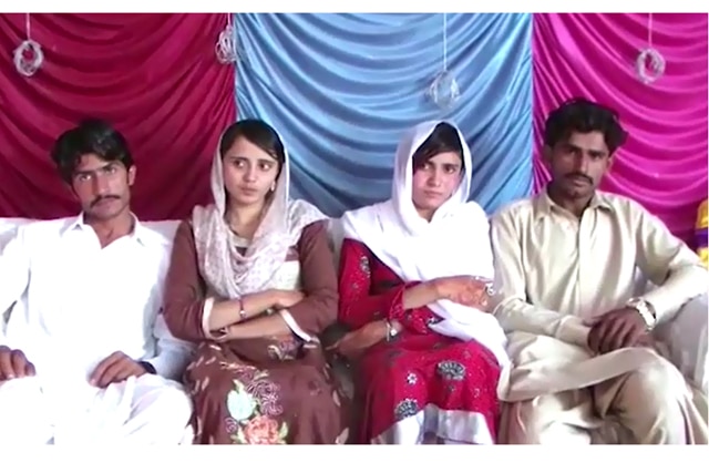 Two girls in head scarves sit on the couch with two men in traditional Pakistani dress.