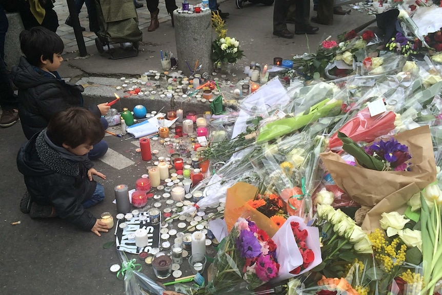 Two children sit beside flowers and candles on the street