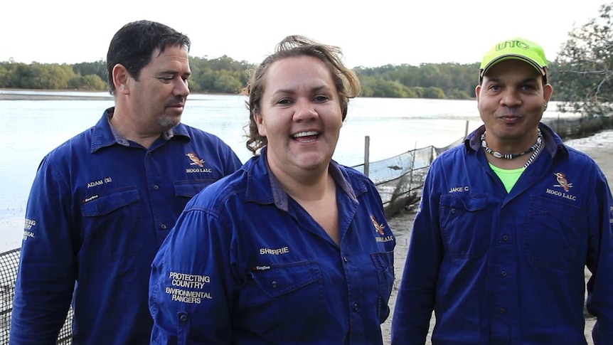 A woman stands in front of two men in front of a river