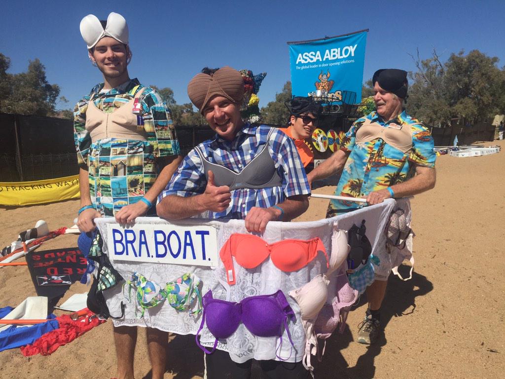 Three men stand in a home-made cardboard boat ready to race down a dry riverbed.