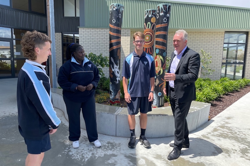 John Freyne, wearing a suit, talks to three students on the school grounds.